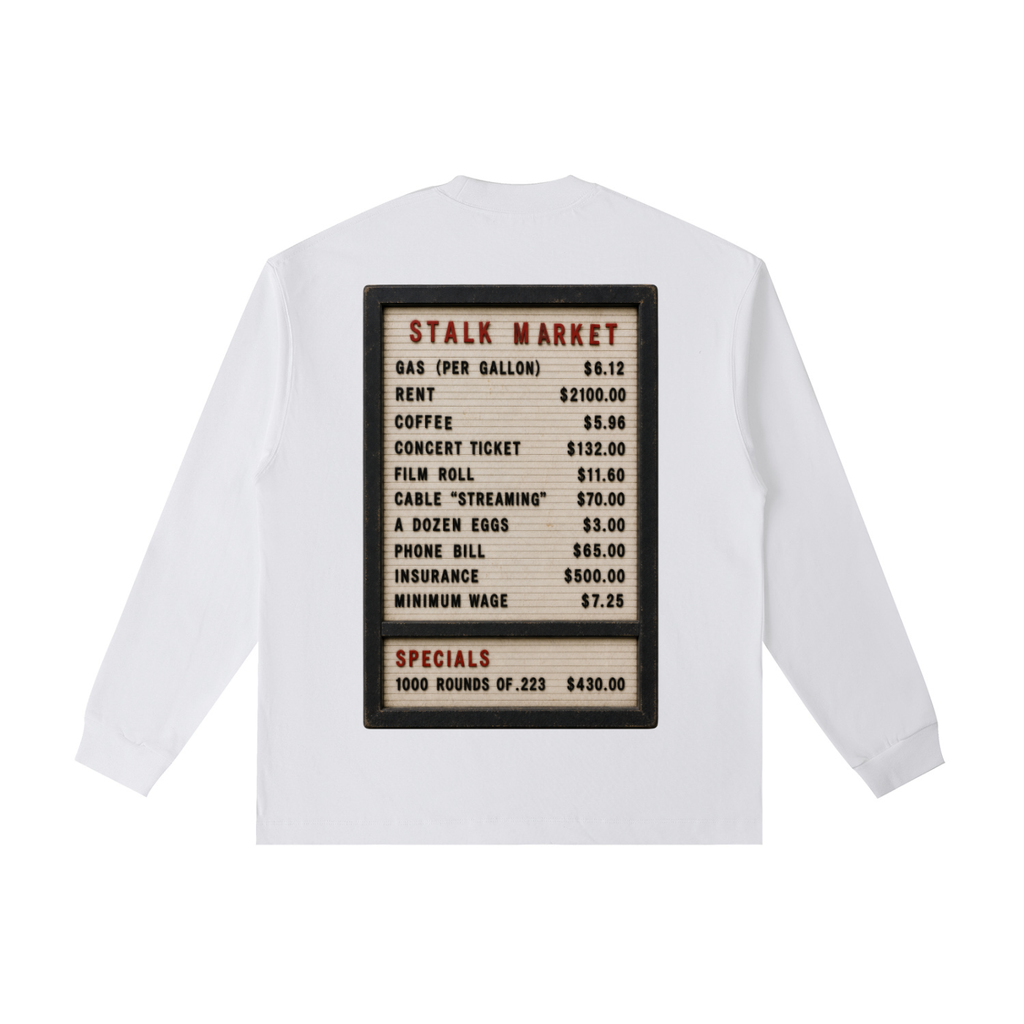 Back view of a white long-sleeve T-shirt featuring a vintage changeable letter board listing consumer prices for gasoline, rent, coffee, concert tickets, wages, and other everyday goods beneath the heading "Stalk Market."