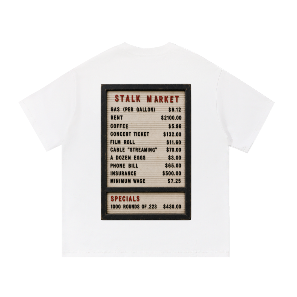 Back view of a white short-sleeve T-shirt featuring a vintage changeable letter board listing consumer prices for gasoline, rent, coffee, concert tickets, wages, and other everyday goods beneath the heading "Stalk Market."